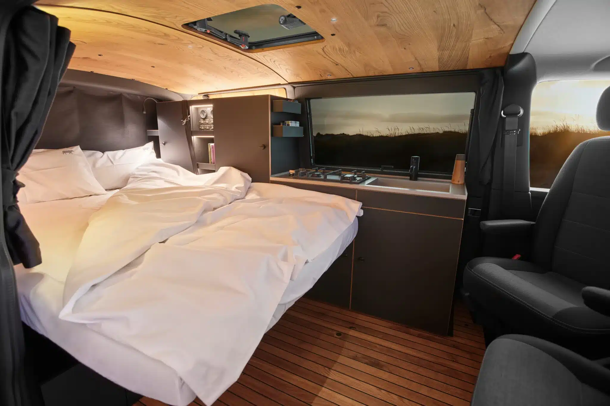 Innenraum eines ausgebauten VW Busses mit schwebendem Bett, kompakter Küche und Holzdekor aus Moormanns Holzklasse 2.0