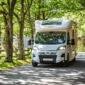 Notin ENVOL Reisemobil fährt auf einer von Bäumen gesäumten Straße durch den Wald.