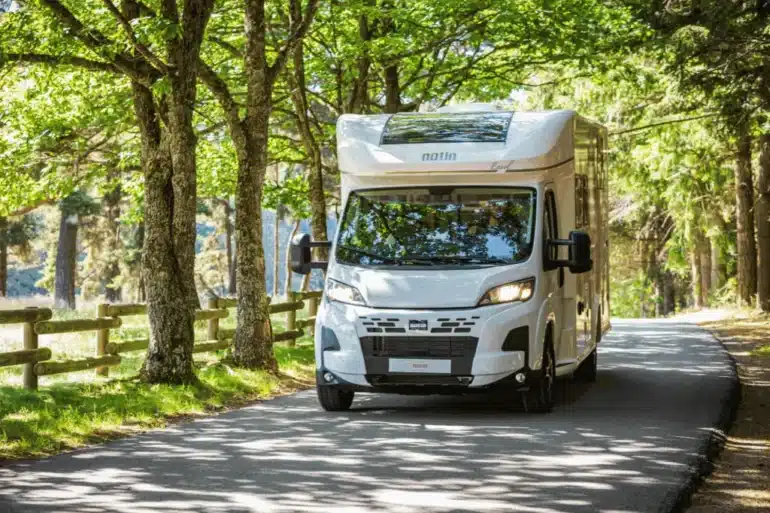 Notin ENVOL Reisemobil fährt auf einer von Bäumen gesäumten Straße durch den Wald.