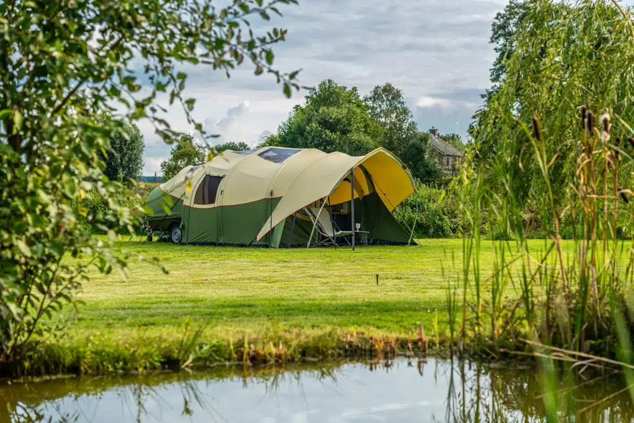Faltcaravan Alpenkreuzer OpenAir mit angebautem Sonnendach auf einem grünen Campingplatz am Teich.
