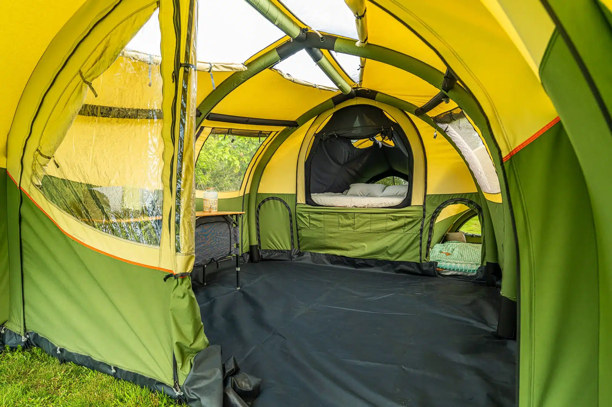 Wohnbereich und Schlafbereich des Alpenkreuzer OpenAir Faltcaravans mit grün-beigem Stoff, offenen Fenstern und Luftgestänge.
