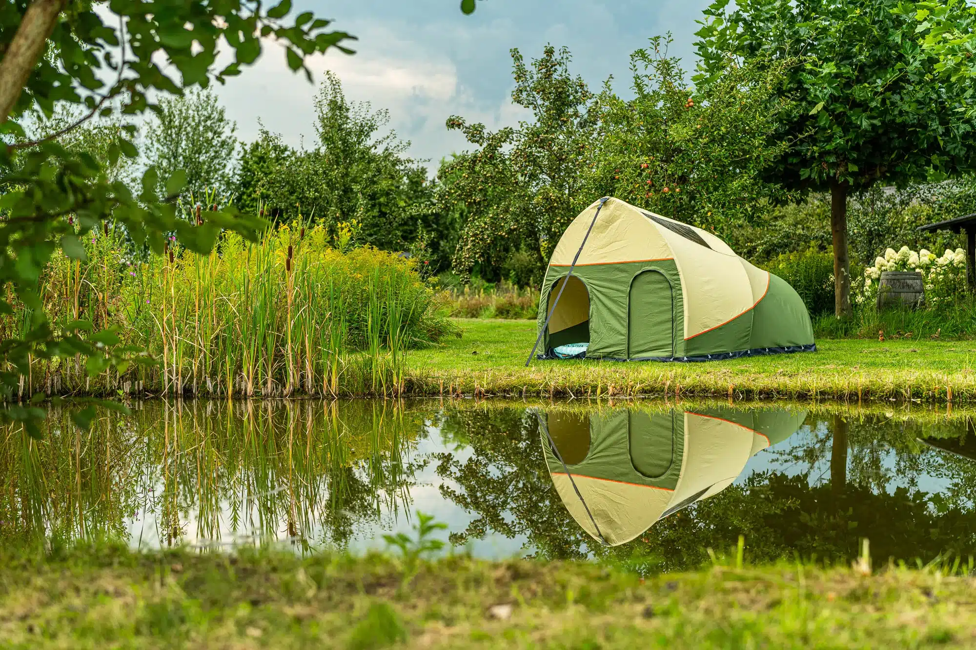 Grünes und beiges Campingzelt steht am Rand eines Teiches im Grünen