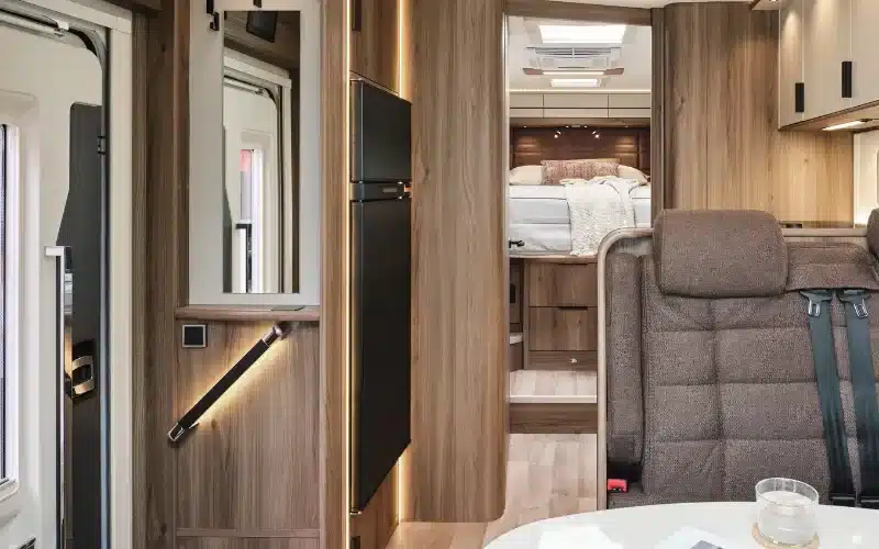 Moderner, heller Innenraum eines KABE Royal x910 LQB mit Sitzgruppe, Kühlschrank und zentralem Mittelgang zum Schlafbereich.