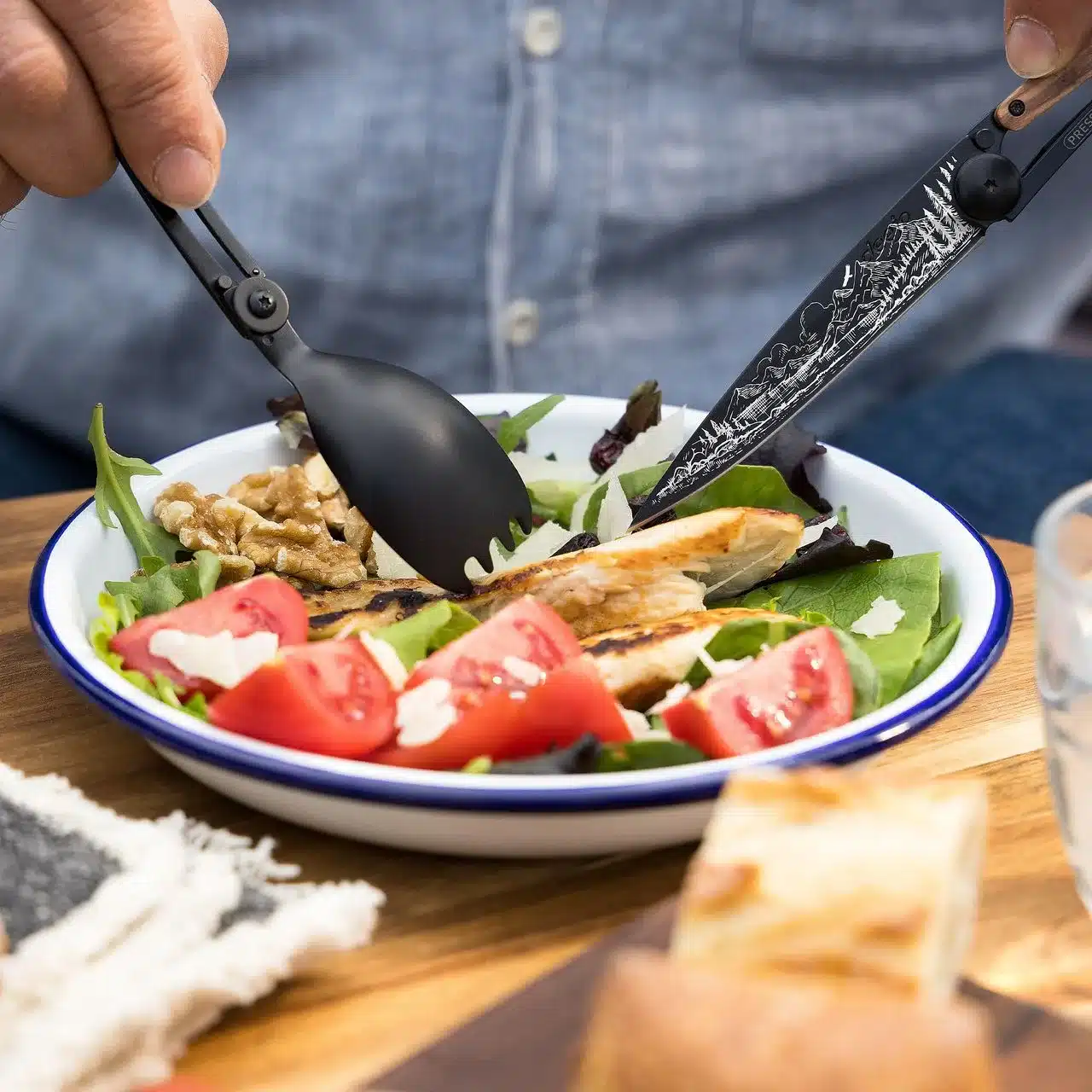 Person isst mit einem schwarzen Spork Deejo 39g und einem Deejo 37g Messer Salat im Freien.