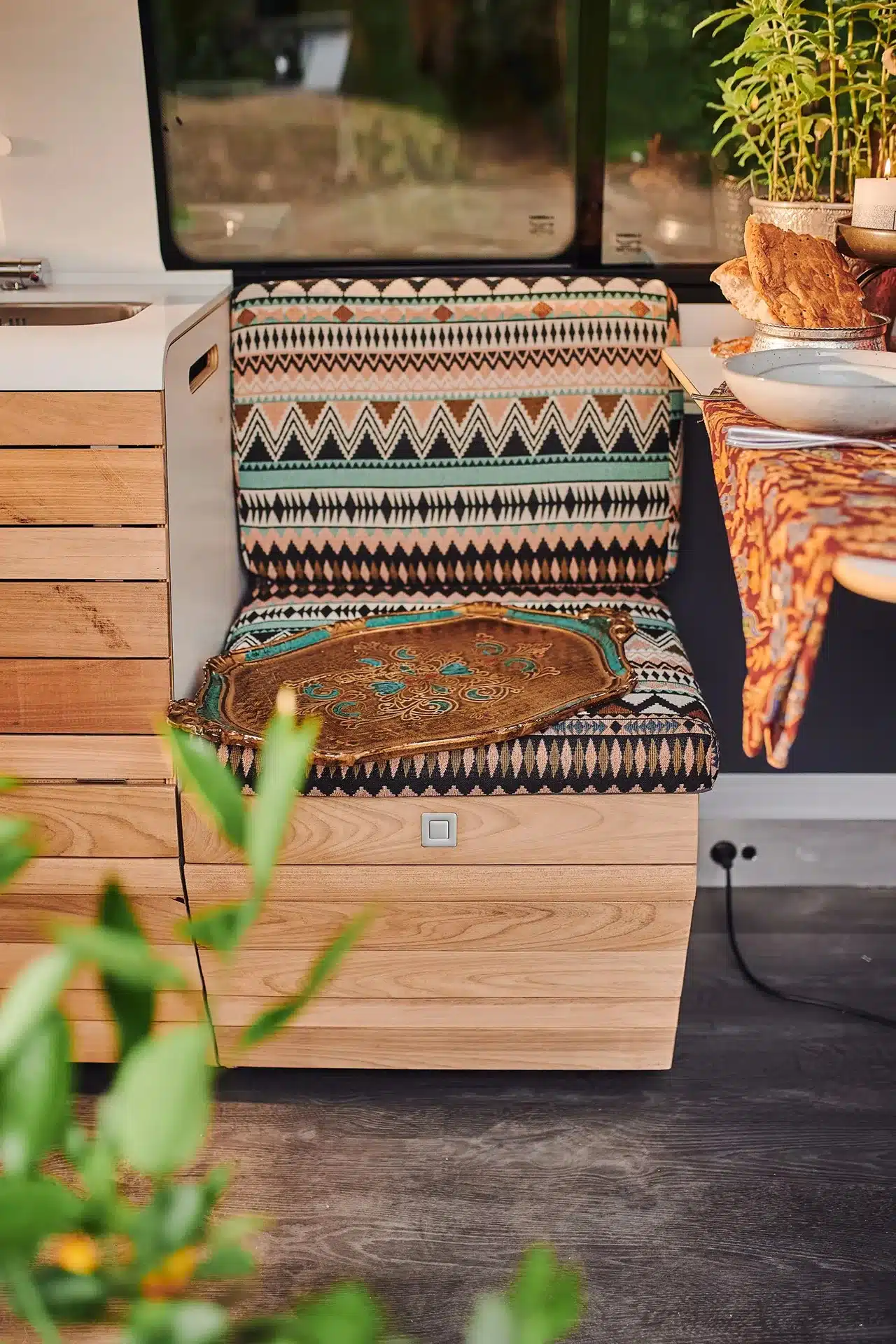 Modulares Sitz- und Küchenelement aus Holz im VAN-Jorn Camper mit gemustertem Polster und Tablett.