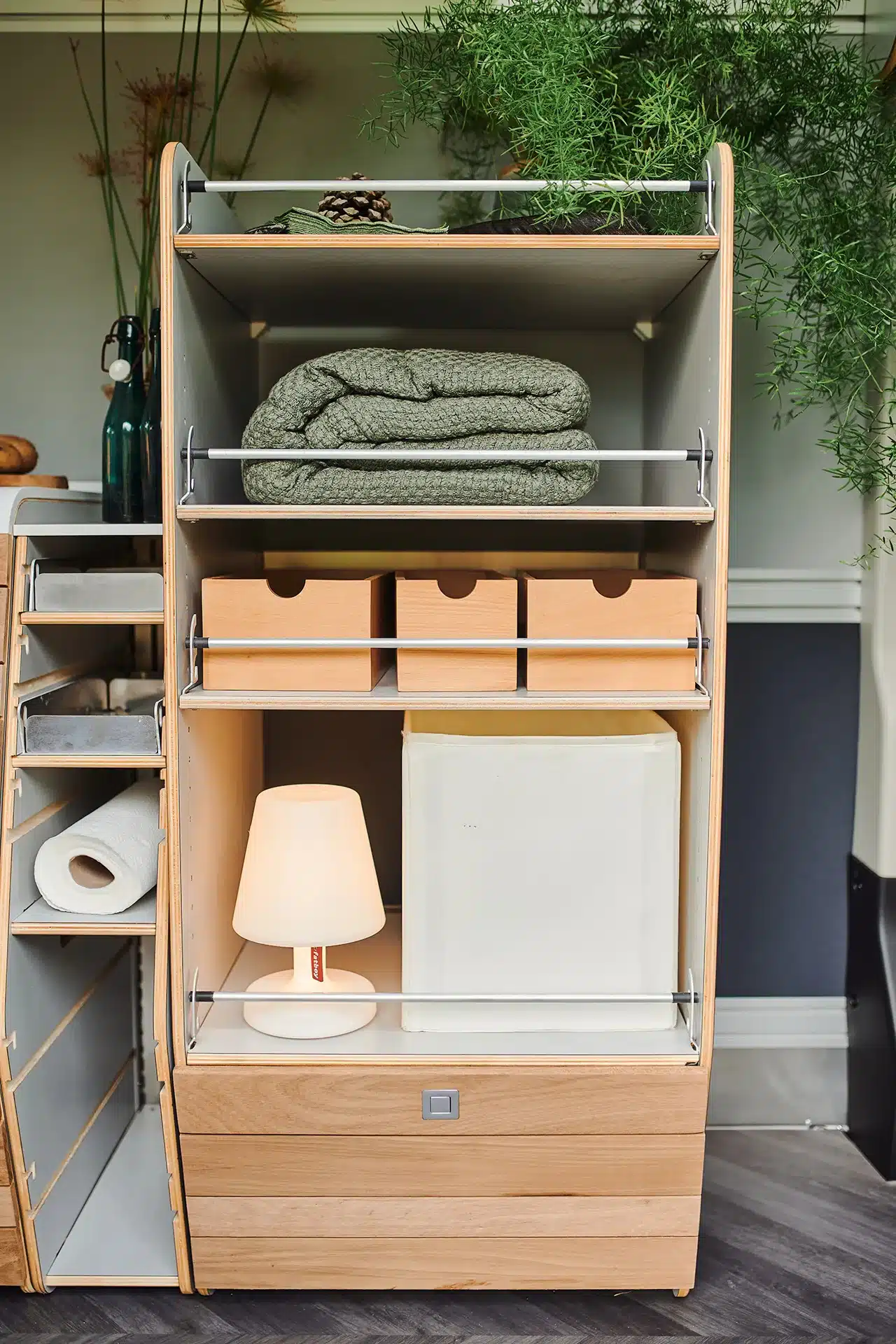 Flexibles Regalsystem mit Holzfächern, Aufbewahrungsboxen und Lampe im Innenraum eines ausgebauten Campers