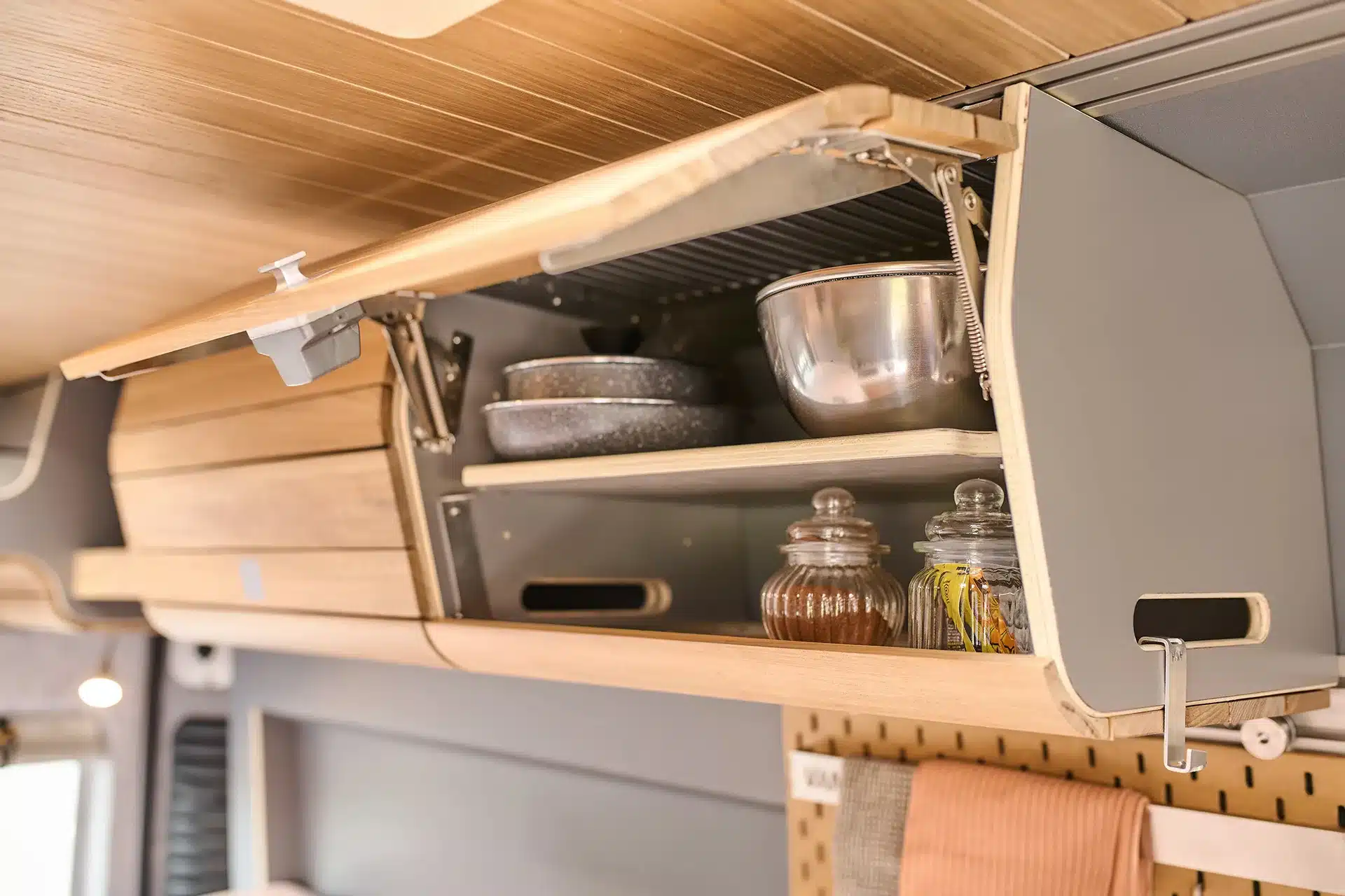 Geöffneter Hängeschrank mit Geschirr, Gläsern und Küchenutensilien im modernen Wohnmobil-Ausbau von VAN-Jorn