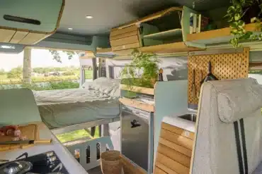 Innenraum eines VAN-Jorn Re:Camp mit Bett, Küchenzeile, Holzschränken und modularen Stauraumlösungen