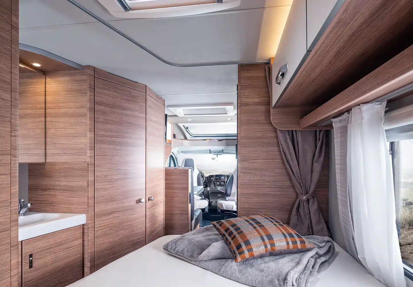 Innenansicht eines WEINSBERG CaraCompact Reisemobils mit Holzmöbeln, Bett, Sitzgruppe und Fenster