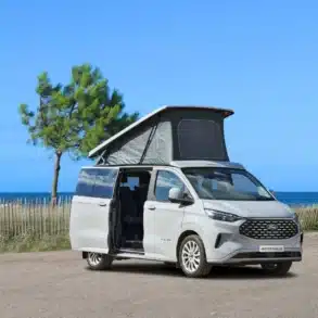 Westfalia Club Joker Urban Campervan mit offenem Aufstelldach, geparkt an einer Küstenstraße mit Meerblick.