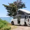 Westfalia Kipling Campervan mit geöffnetem Aufstelldach an einem Seeufer, im Hintergrund Wasser und Bäume