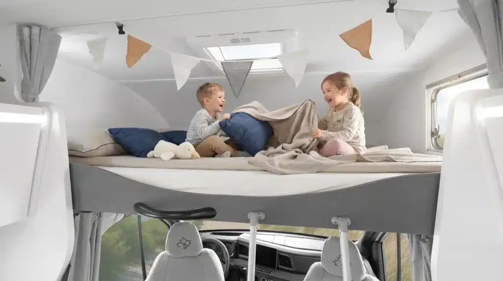 Innenraum eines Alkoven-Reisemobils mit zwei Kindern im Alkovenbett über dem Fahrerhaus