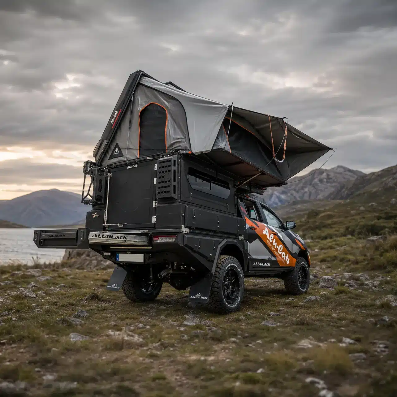 Pick-up-Fahrzeug mit AluBlack Flatbed, Dachzelt und modularen Staufächern in felsiger Landschaft