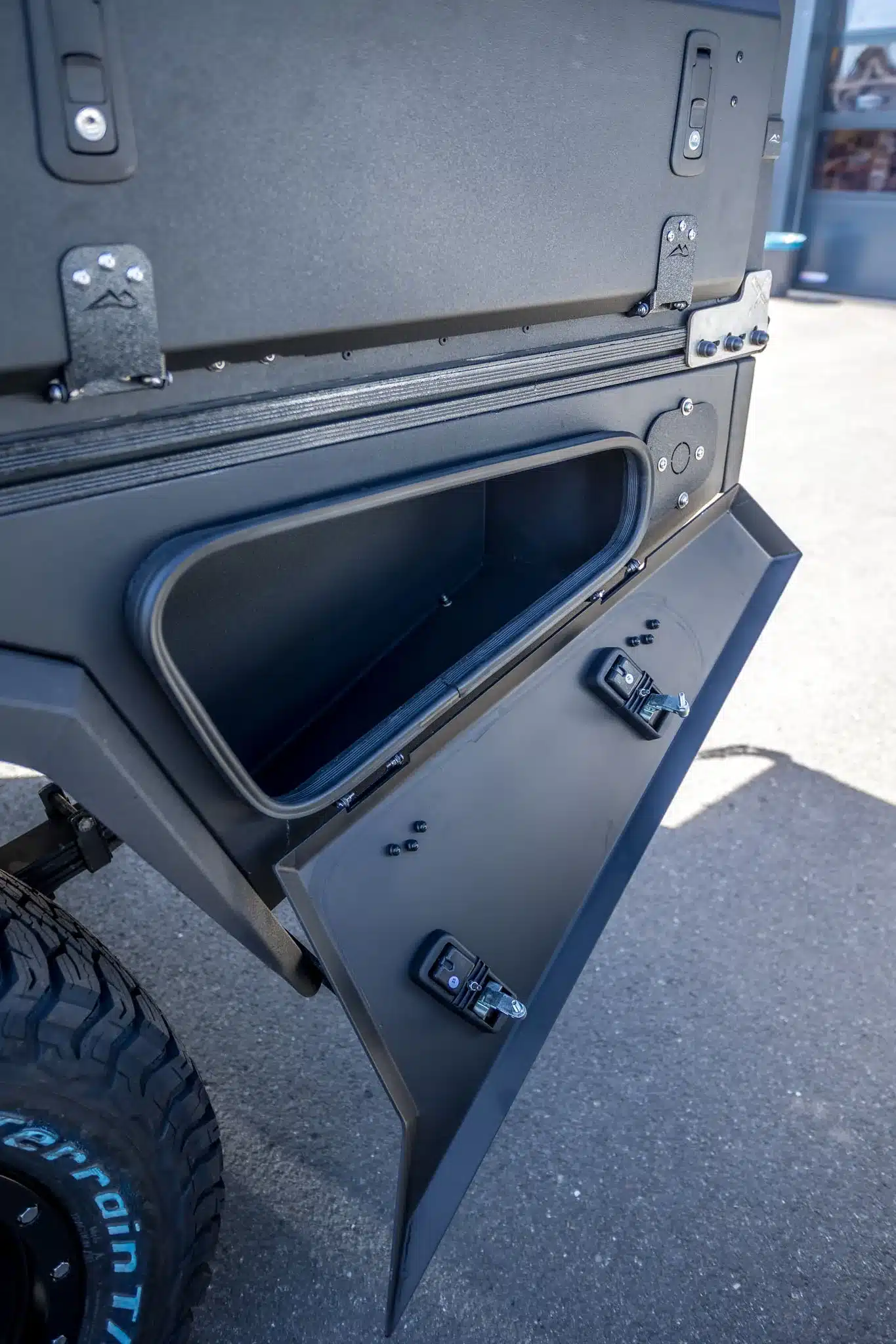 Geöffnetes seitliches Staufach an einem AluBlack Flatbed Pick-up-Umbau mit robuster Aluminiumkonstruktion.