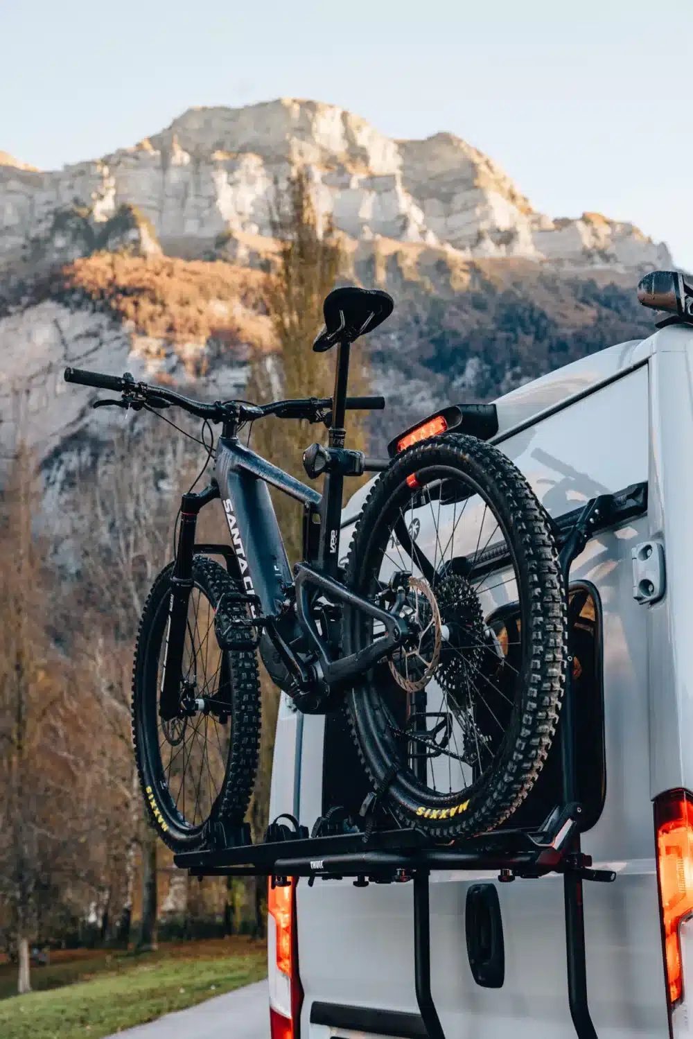 Zwei Mountainbikes auf dem Fahrradträger eines weißen Camper Vans vor einem Berg