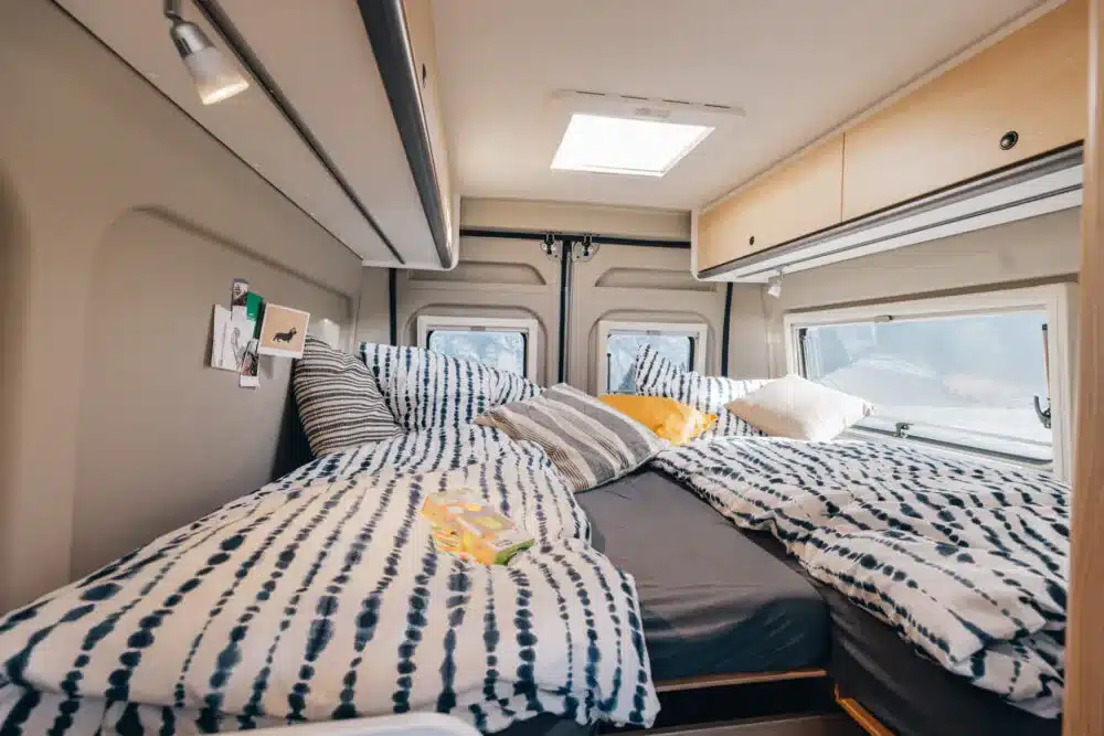 Schlafbereich im Sunlight CLIFF Adventure Camper Van mit zwei Liegeflächen, Bettwäsche und Oberschränken