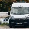 Weißer Sunlight CLIFF 540 Camper Van von Peugeot steht an einem See vor einem Wald