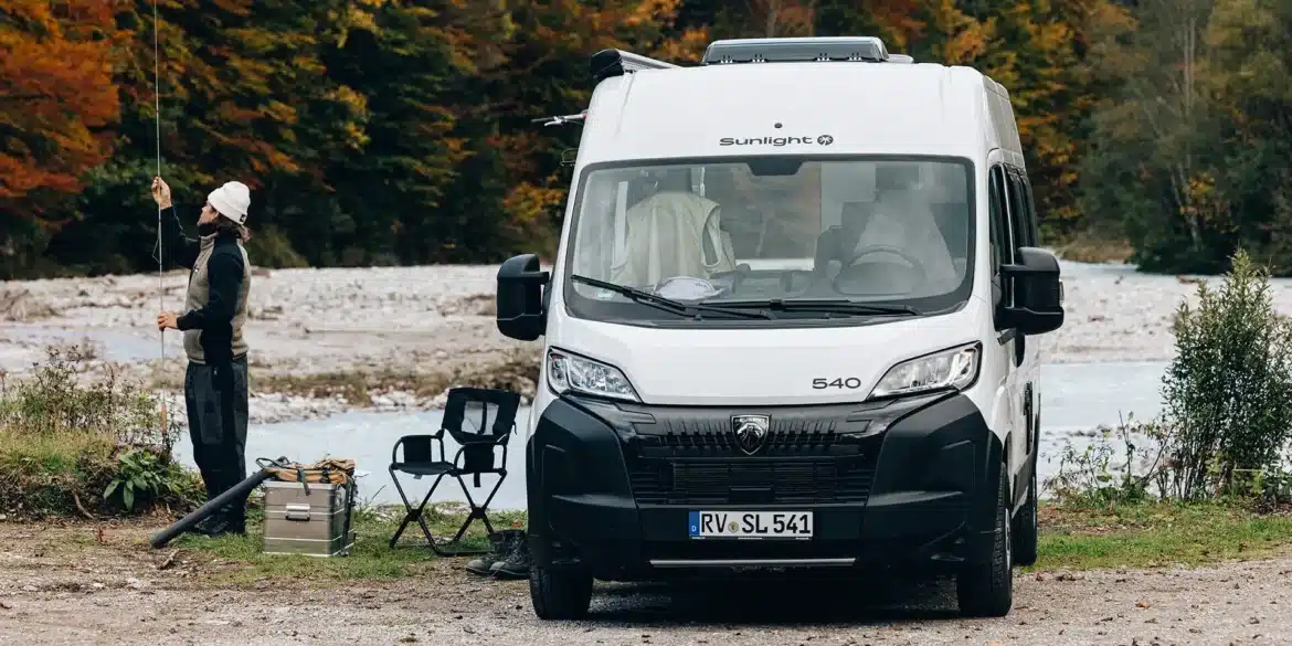 Weißer Sunlight CLIFF 540 Camper Van von Peugeot steht an einem See vor einem Wald