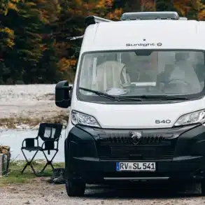 Weißer Sunlight CLIFF 540 Camper Van von Peugeot steht an einem See vor einem Wald