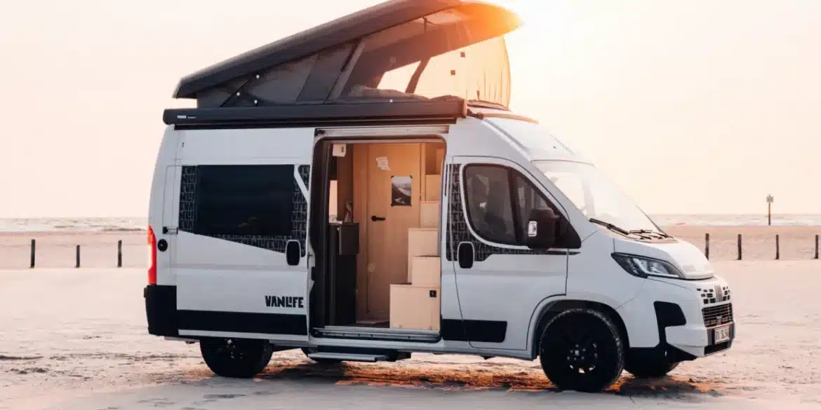 Weißer Sunlight CLIFF VANLIFE Camper Van mit geöffnetem Schlafdach und Schiebetür am Strand
