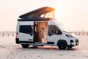 Weißer Sunlight CLIFF VANLIFE Camper Van mit geöffnetem Schlafdach und Schiebetür am Strand