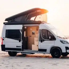 Weißer Sunlight CLIFF VANLIFE Camper Van mit geöffnetem Schlafdach und Schiebetür am Strand