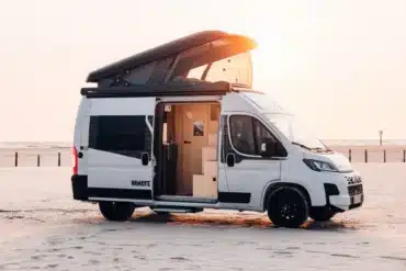Weißer Sunlight CLIFF VANLIFE Camper Van mit geöffnetem Schlafdach und Schiebetür am Strand