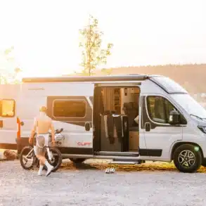 Sunlight CLIFF X Kastenwagen-Camper geöffnet, ein Mann mit Fahrrad am See bei Sonnenaufgang