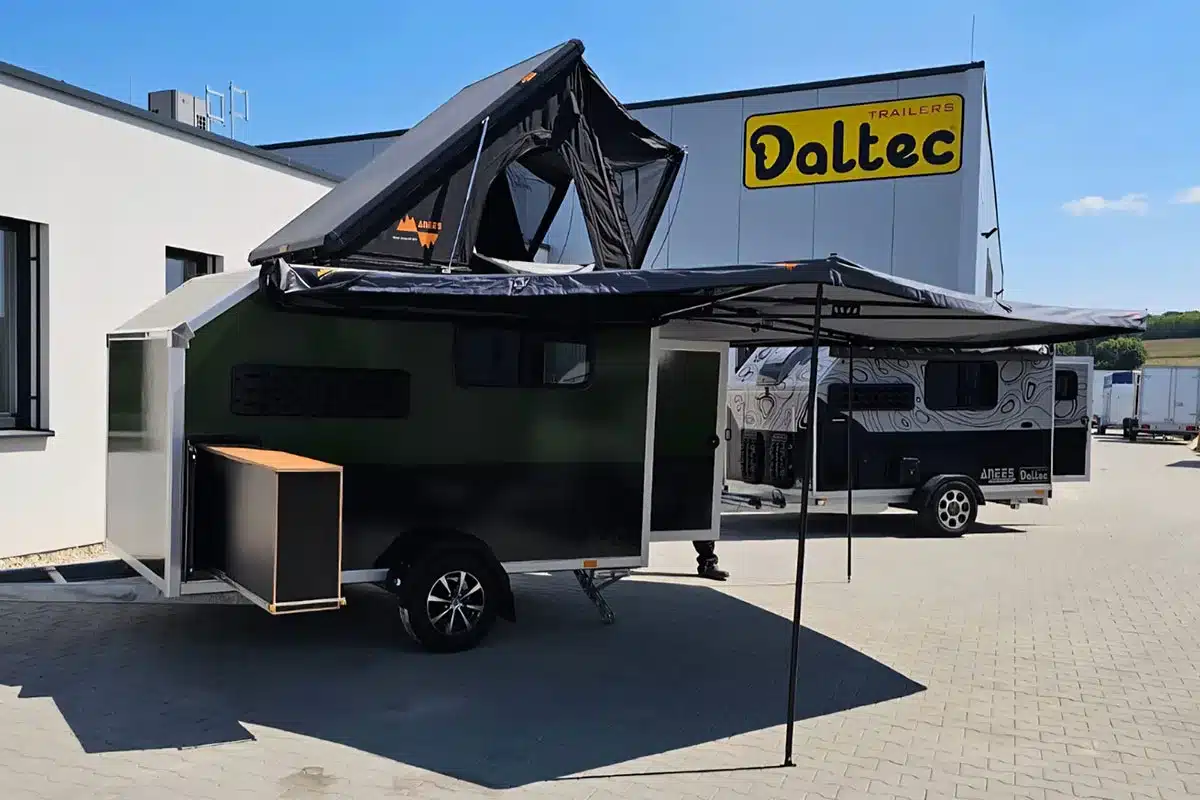 Daltec D’ Camper Campinganhänger mit Dachzelt und ausgefahrener Markise vor einem Herstellergebäude