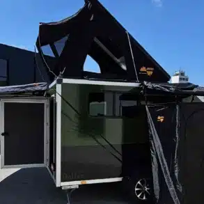 D’ Camper Campinganhänger mit geöffnetem Dachzelt, Markise und Seitenzelt auf einem Betriebsgelände