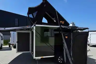 D’ Camper Campinganhänger mit geöffnetem Dachzelt, Markise und Seitenzelt auf einem Betriebsgelände