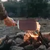 Hand hält das Donkey Long Tong Paddel über ein brennendes Lagerfeuer.