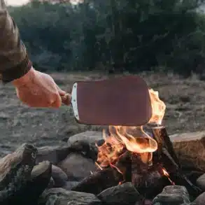 Hand hält das Donkey Long Tong Paddel über ein brennendes Lagerfeuer.