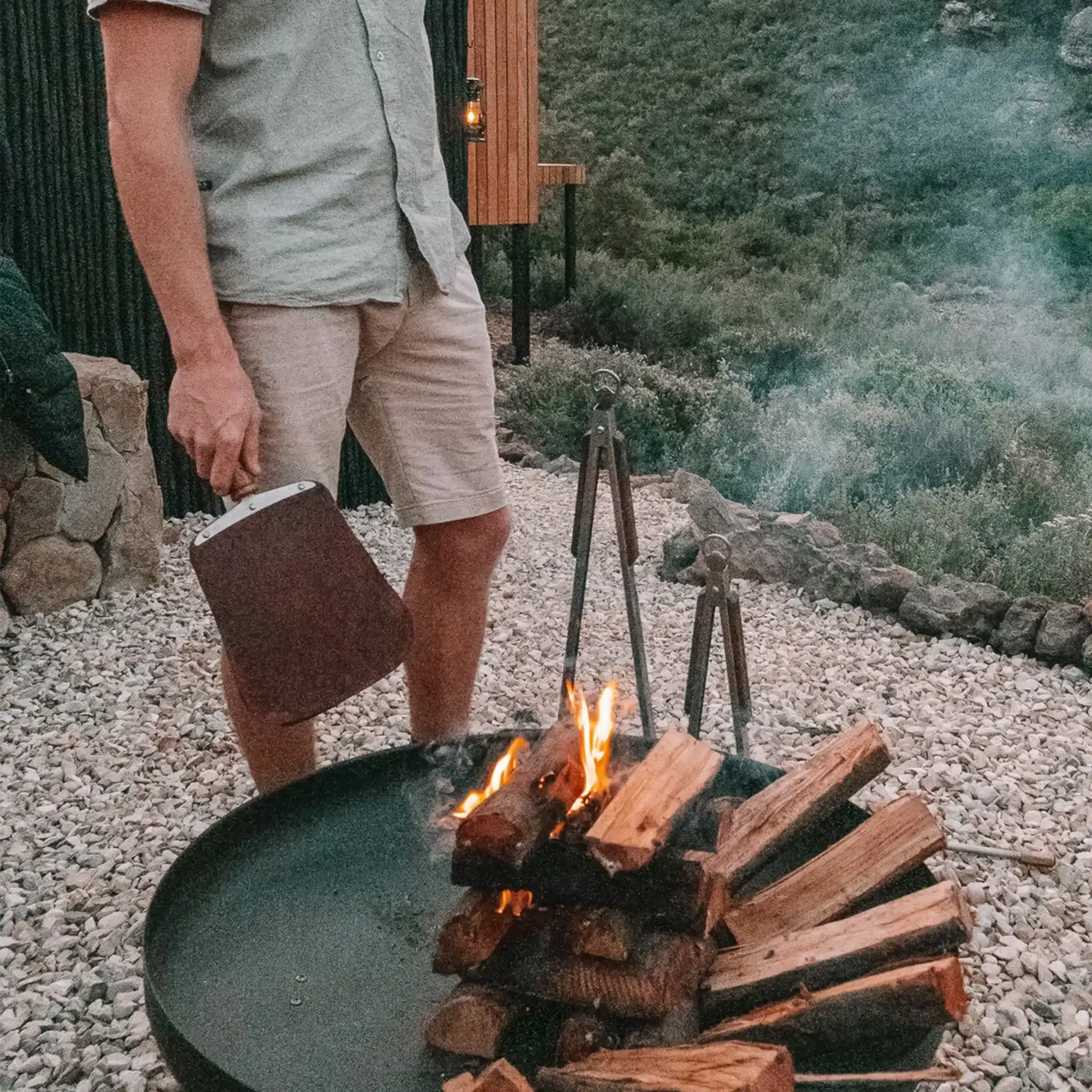 Person hält das Donkey Long Tong Paddel aus Leder und Federstahl an einer Feuerschale beim Camping.