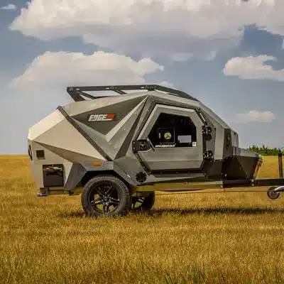 EdgeOut Teardrop-Camper mit kantiger Außenhülle, Dachträger und Offroad-Reifen auf einer Wiese