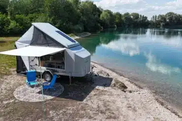 Farfalla Camper flip mit geöffnetem Aufstelldach und Markise an einem Seeufer