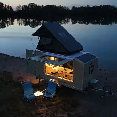 Farfalla Camper flip mit geöffnetem Panoramadach und Dachzelt am Seeufer, Campingstühle davor, Abendstimmung.