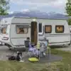 Weißer Fendt-Caravan APERO 515 mit geöffneter Tür an einem See vor einer Bergkulisse