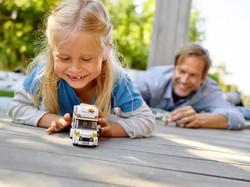 Kind spielt mit dem LEGO City Ferien-Wohnmobil 60283 auf einer Holzterrasse.