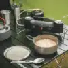 Der Fire Finch Double Stove von Robens steht als mobiler Campingkocher mit zwei Brennern und Windschutz auf einem Campingtisch.