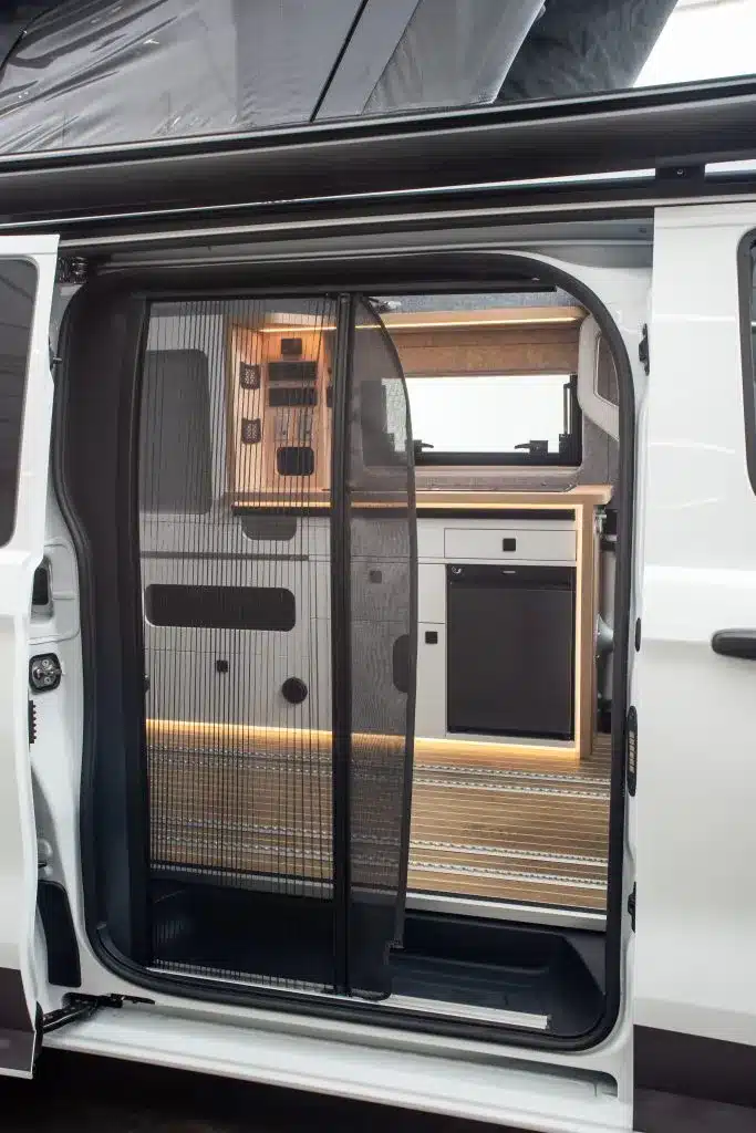 Offene Schiebetür eines Ford Custom 4x4 Wavecamper, Blick auf Küchenzeile und Fliegengitter im Einstieg.