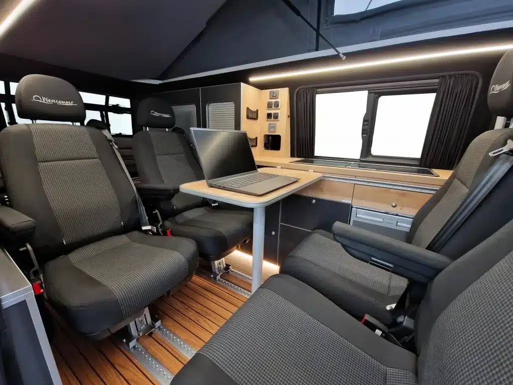 Innenraum des Ford Custom 4x4 Wavecamper mit vier Einzelsitzen auf Schienen, Tisch und Küchenzeile.