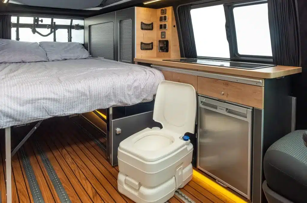 Innenraumansicht des Ford Custom 4x4 Wavecamper mit Bett, Küchenzeile, Kühlschrank und tragbarer Toilette