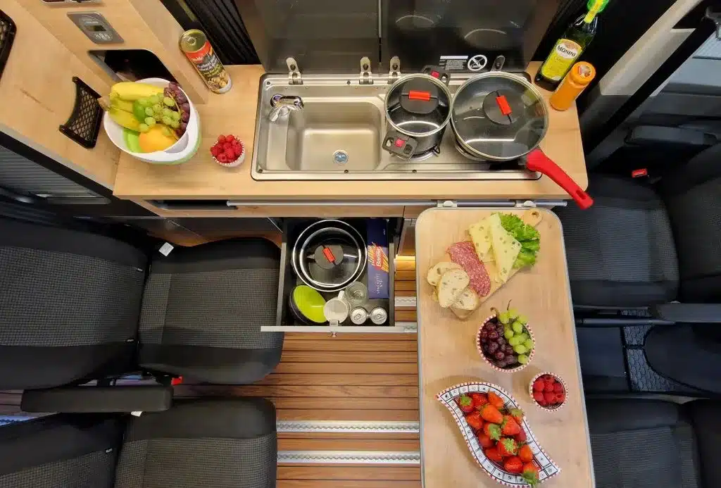 Camperküche und Sitzbereich im Ford Custom 4x4 Wavecamper mit Tisch, Spüle und Lebensmitteln