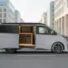 Grauer Ford Custom Flex von Wavecamper mit geöffneter Schiebetür und integrierter Campingküche in einer Stadtstraße