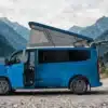 Blauer Ford Custom Flex E-Line Campervan mit geöffnetem Aufstelldach vor einer alpinen Berglandschaft