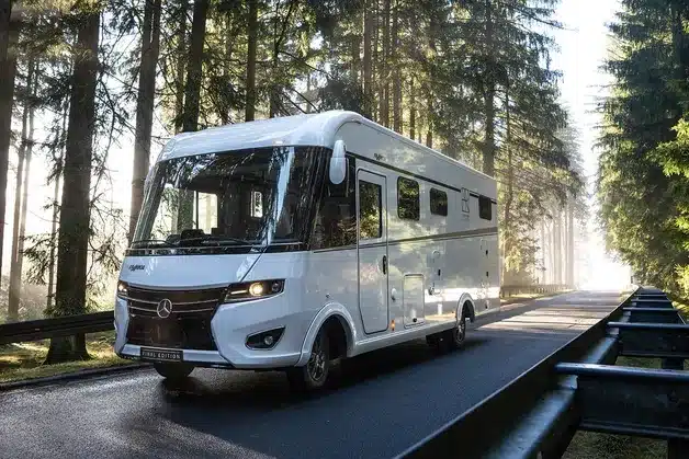 Weißes FRANKIA FINAL EDITION Reisemobil auf Mercedes-Benz-Basis fährt durch einen Wald.