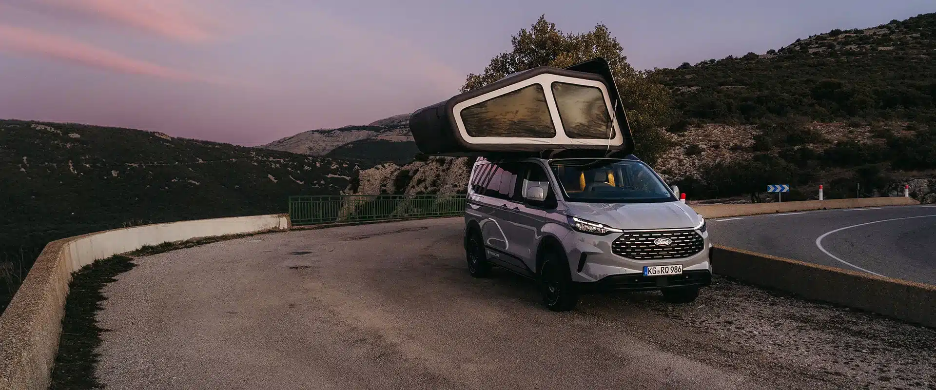 Freescape Adventure Line Campervan mit aufgeklapptem, aufblasbarem Schlafdachzelt auf einer Bergstraße bei Sonnenuntergang.