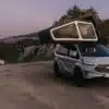 Der Freescape Street Line Campervan mit aufgeklapptem, aufblasbarem Dachzelt steht auf einer Straße in Gebirgslandschaft.