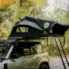 Geöffnetes Go Overland Voyage Hybrid-Dachzelt auf einem Geländewagen mit Leiter und seitlichen Fenstern im Wald.